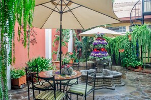 Un patio con una mesa redonda, sillas, una fuente de piedra y diferentes macetas con plantas.