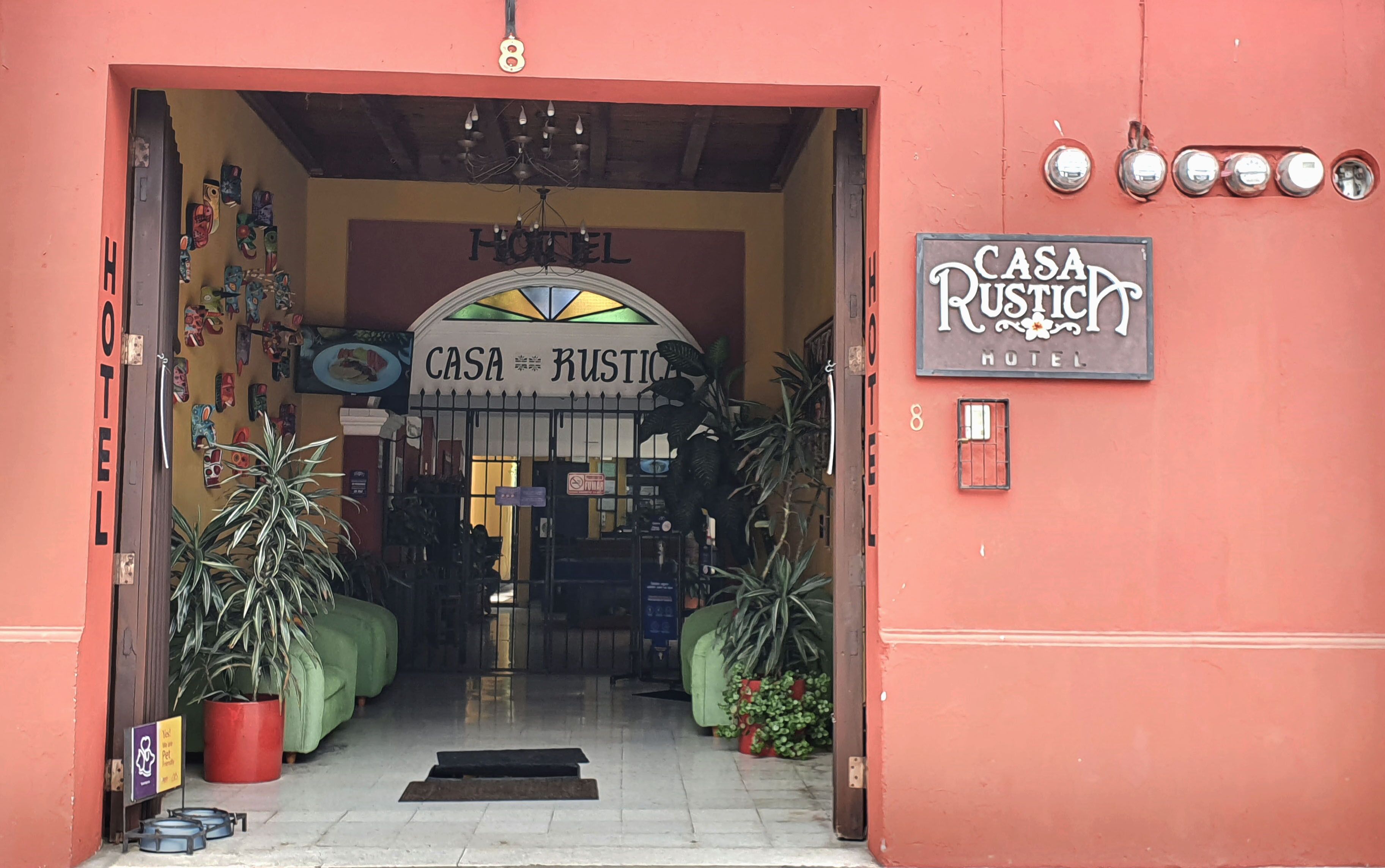 The entrance to Casa Rustica Hotel, featuring a welcoming archway, a signboard, and potted plants.