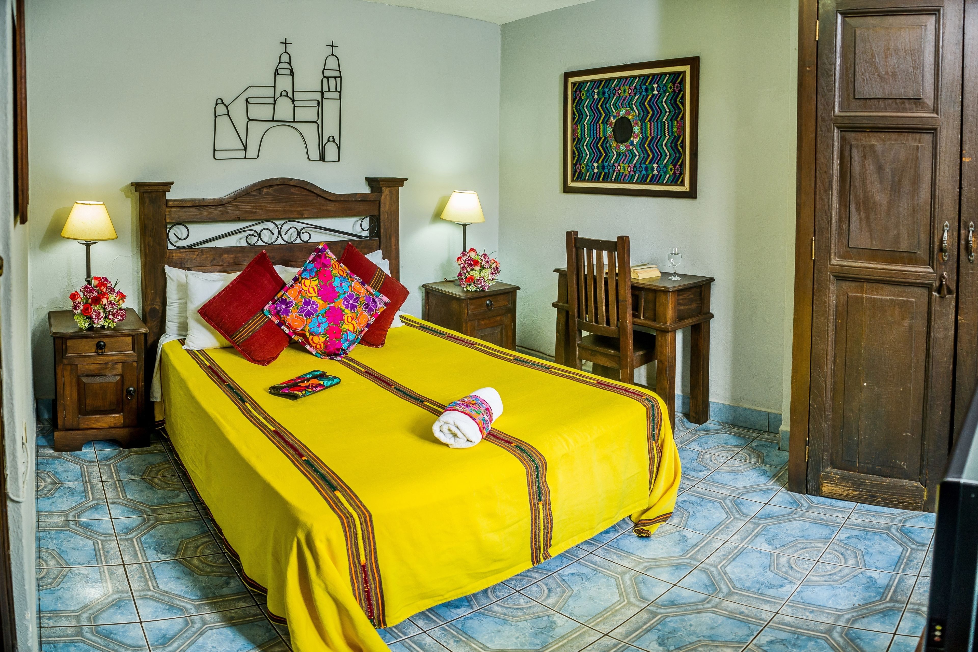 Una habitación de hotel con una cama, dos mesitas de noche, una silla de madera, un armario de madera y una puerta.
