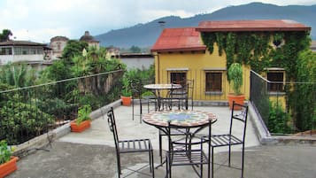 Terraza en la azotea con una mesa redonda y sillas, rodeada de plantas en macetas y vistas a una montaña.