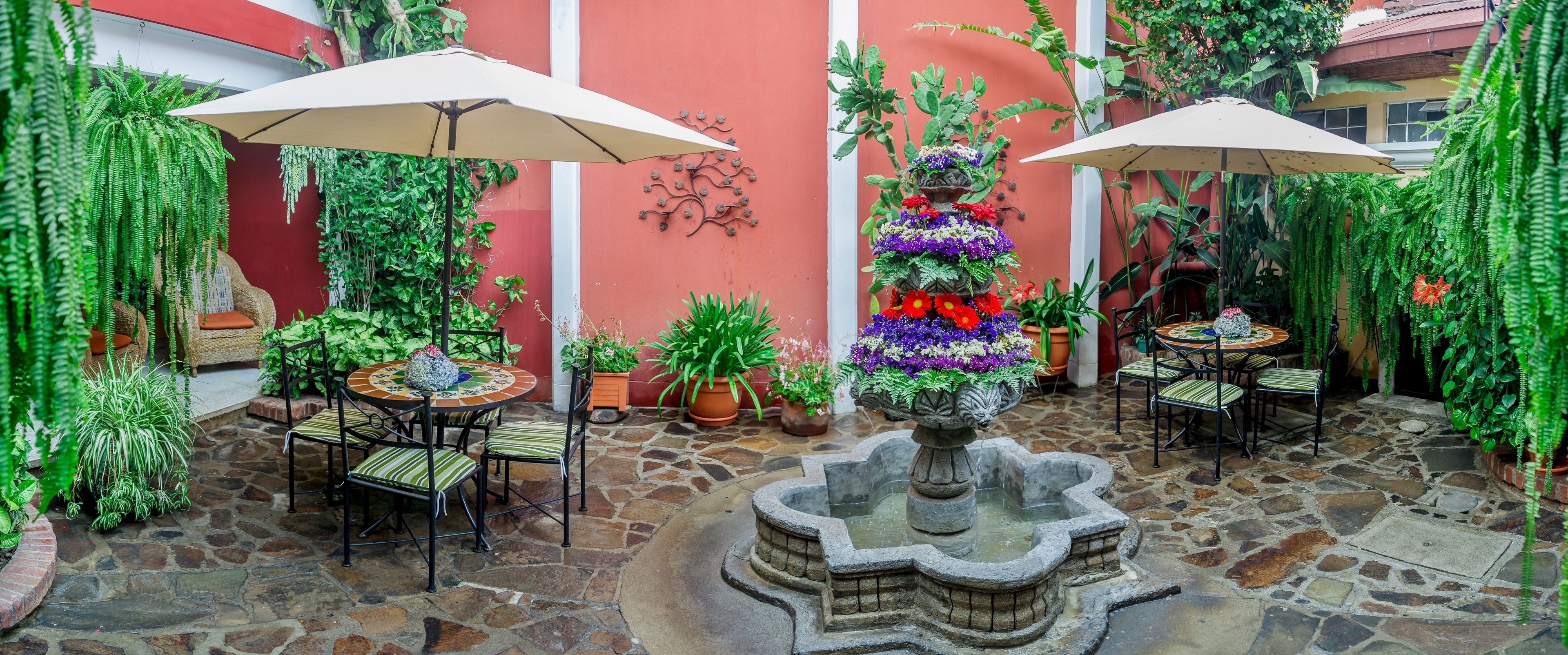 Une cour avec un sol en pierre, deux tables rondes avec des chaises et des plantes en pot.