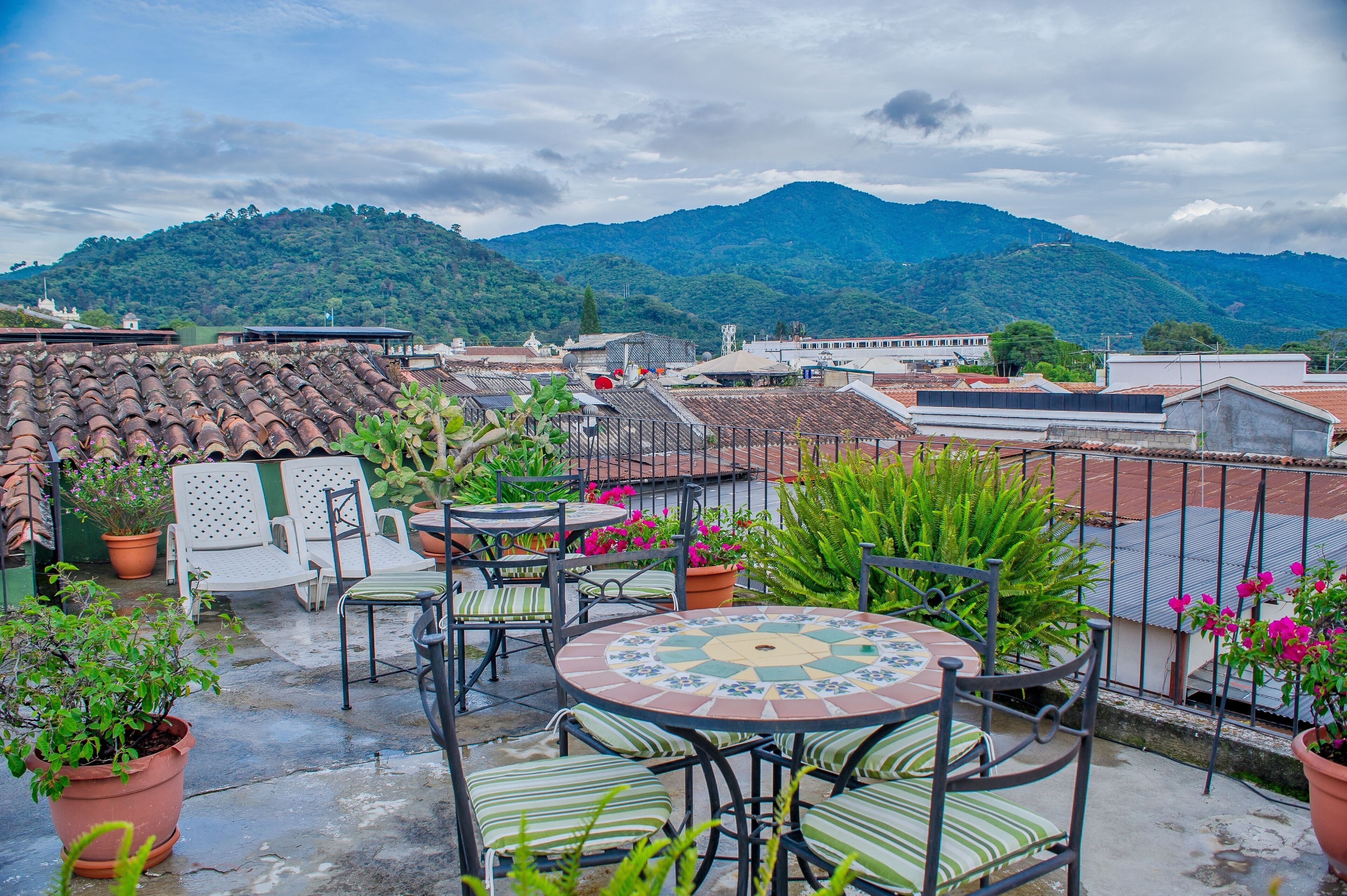 A rooftop terrace with outdoor seating, potted plants, and a view of a mountain.