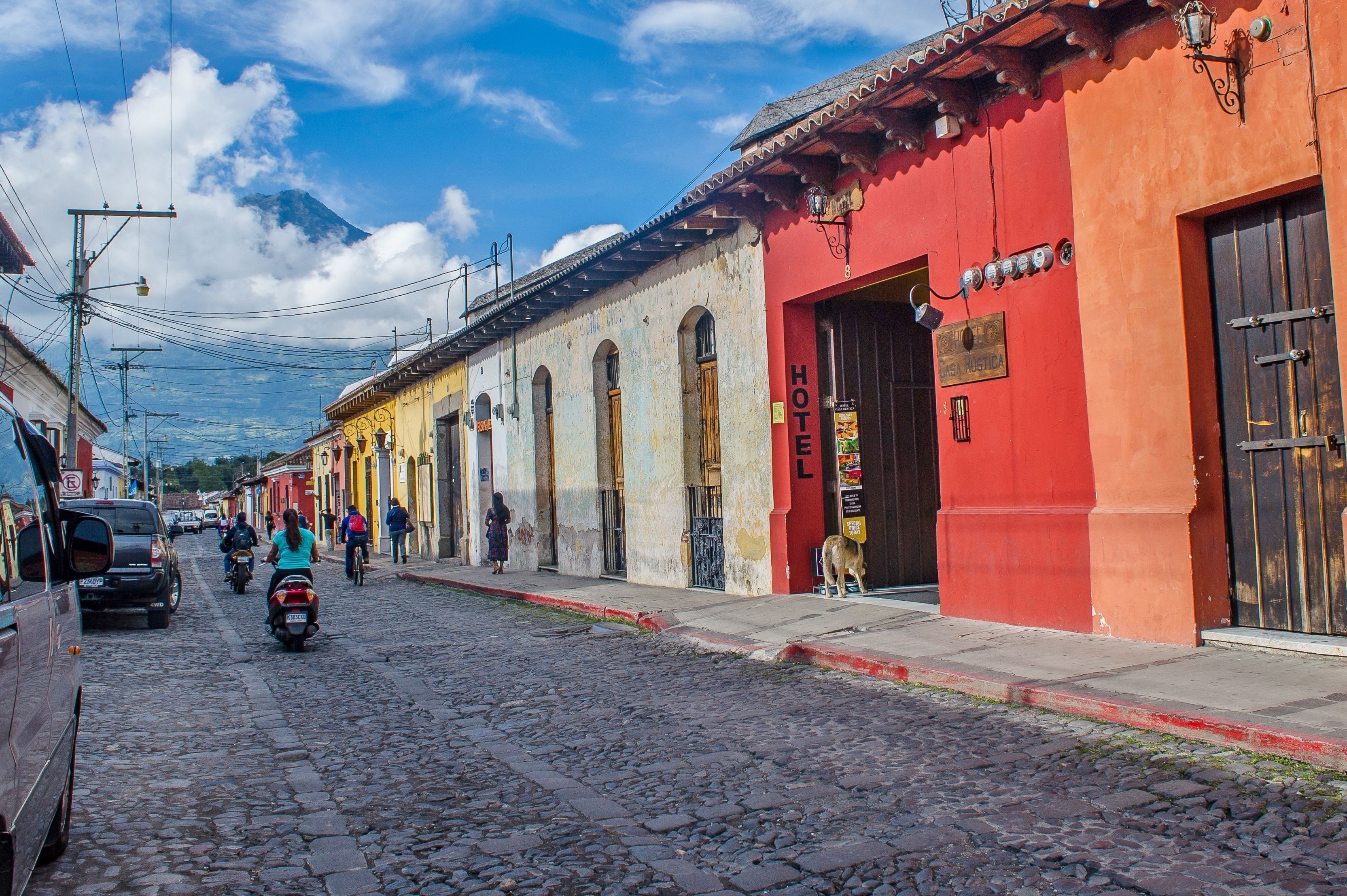 Una calle adoquinada flanqueada por edificios coloridos, incluyendo un edificio rojo con un letrero que dice 'HOTEL'.