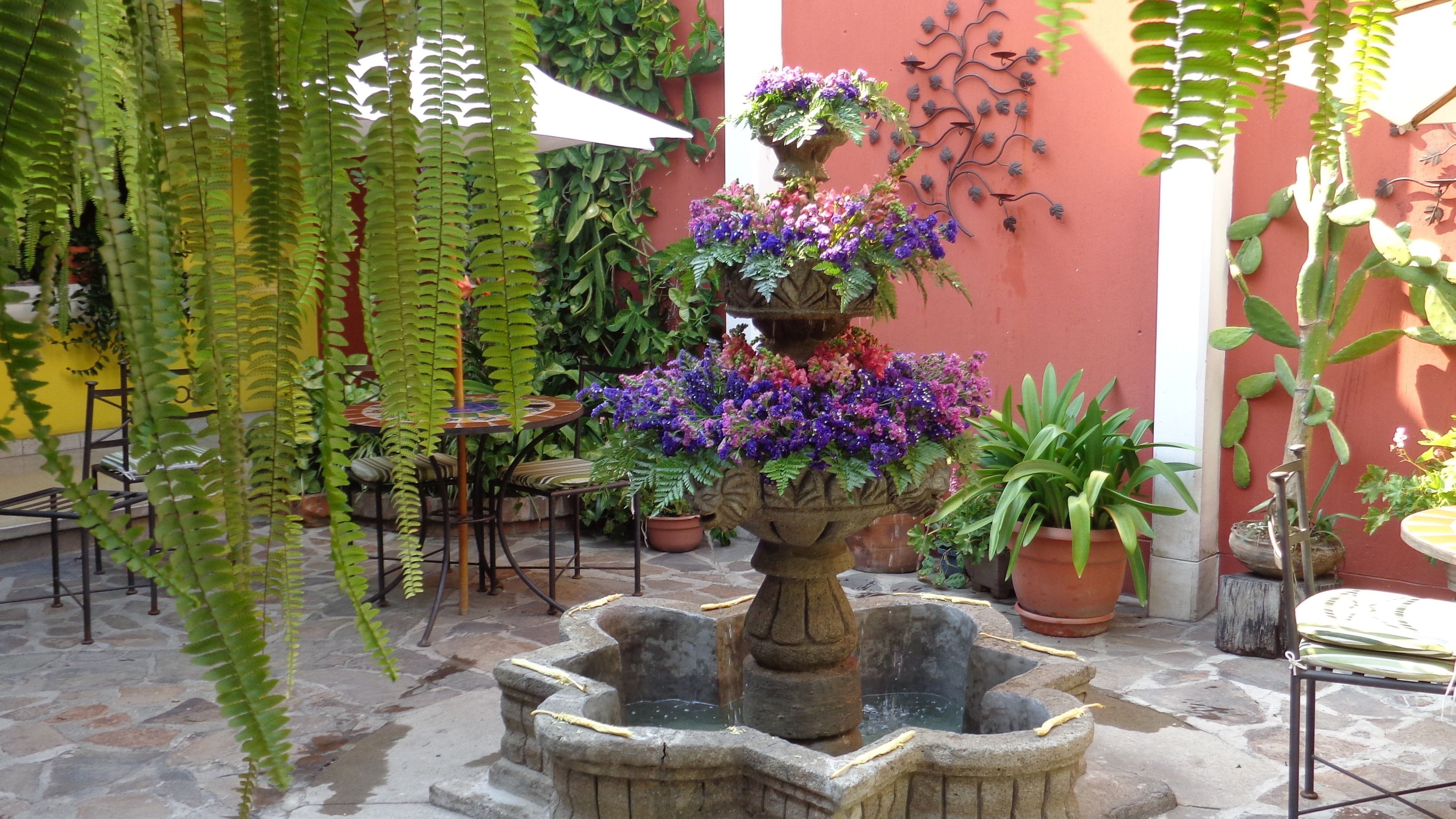 Une cour avec une fontaine en pierre, des plantes en pot et des sièges d’extérieur.