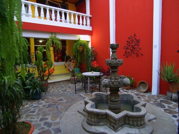 Un patio con una fuente de piedra, plantas en macetas y una mesa con sillas.