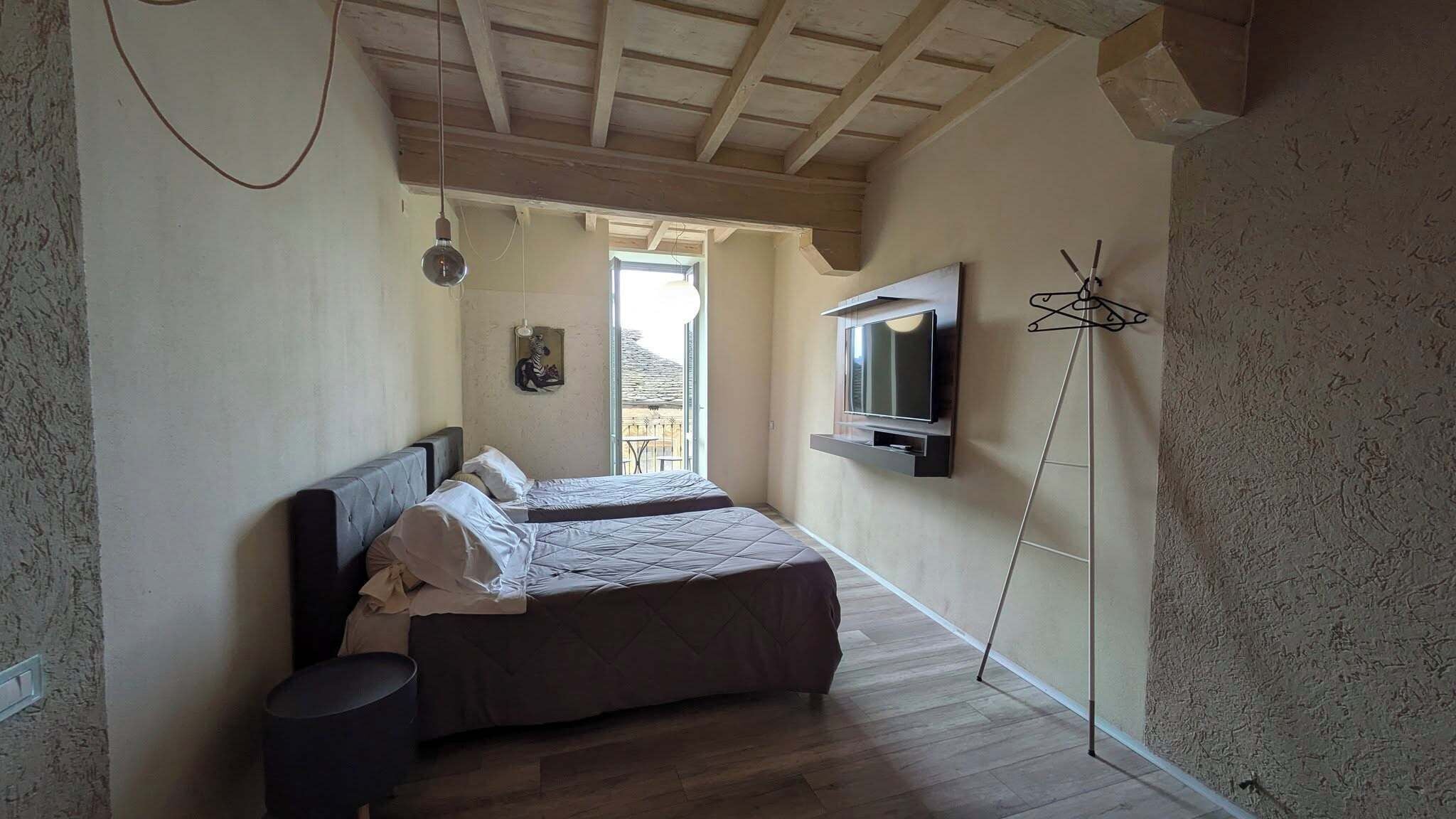 Ein Schlafzimmer mit zwei Betten, einem an der Wand befestigten Fernseher und einem Balkon mit Aussicht.