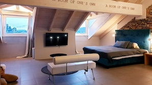 Une chambre confortable située dans les combles, avec un grand lit, un banc, une télévision et un mur en pierre.