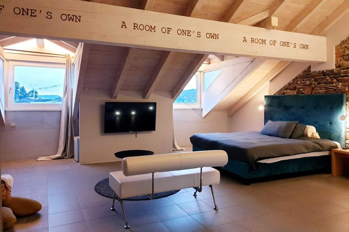 A cozy attic bedroom with a large bed, a bench, a TV, and a stone wall.