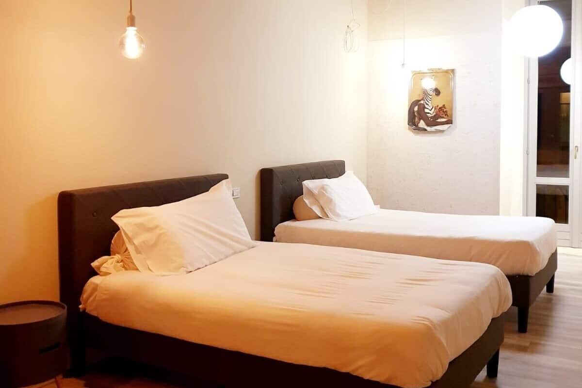 A hotel room with two beds, a round side table, and a wall-mounted light fixture.