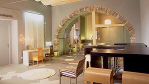 Un salon moderne avec une arche en pierre menant à un espace cuisine. On y trouve plusieurs chaises et une table à manger, une cheminée et une grande fenêtre.