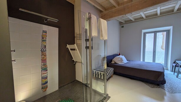 A bedroom with a bed, a glass shower enclosure, and a bathroom with a tiled wall. - Hotel Aracoeli (Orta San Giulio)