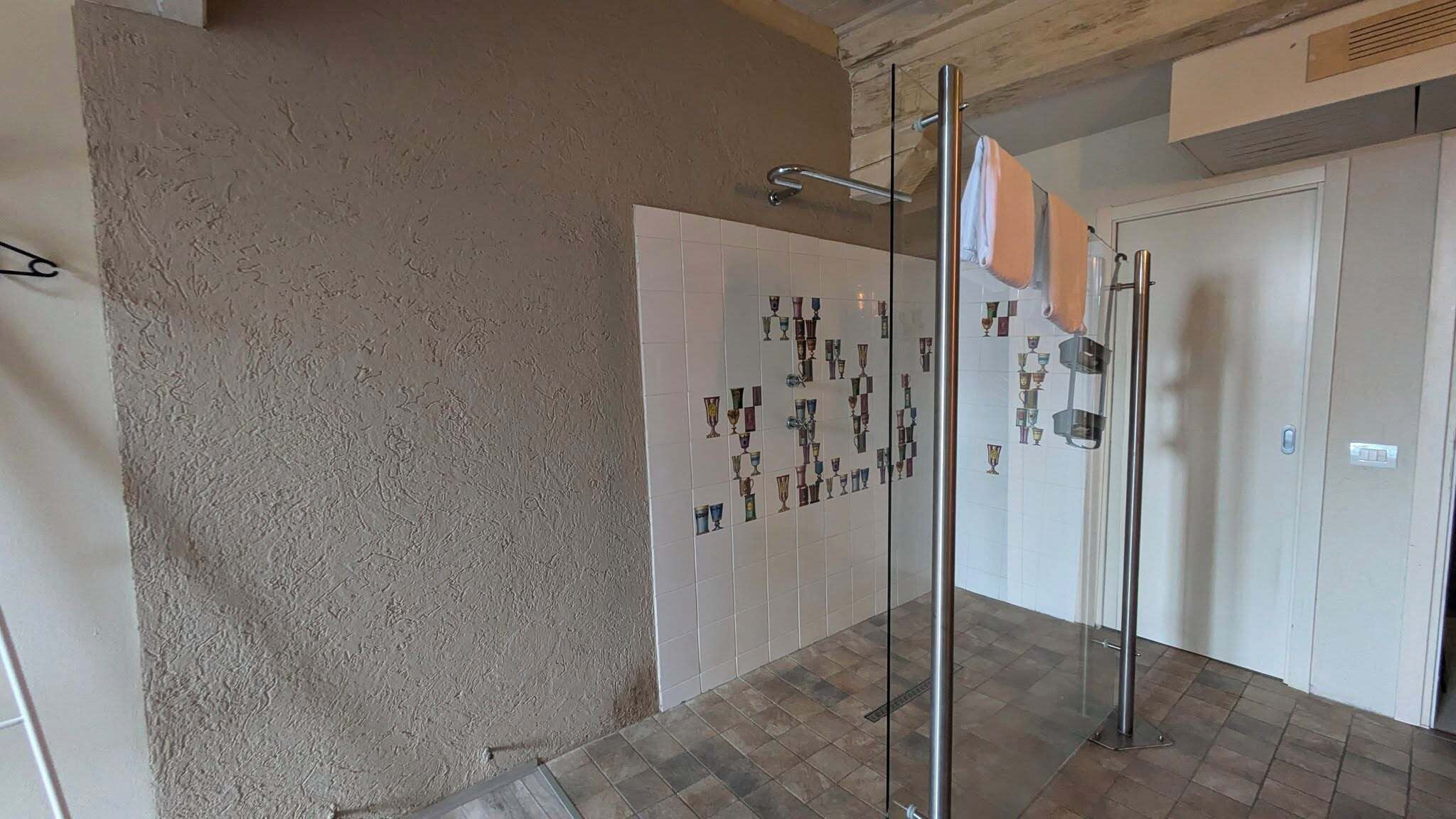 Un baño con pared texturizada, suelo de baldosas y cabina de ducha con mampara de vidrio y un perchero para toallas.