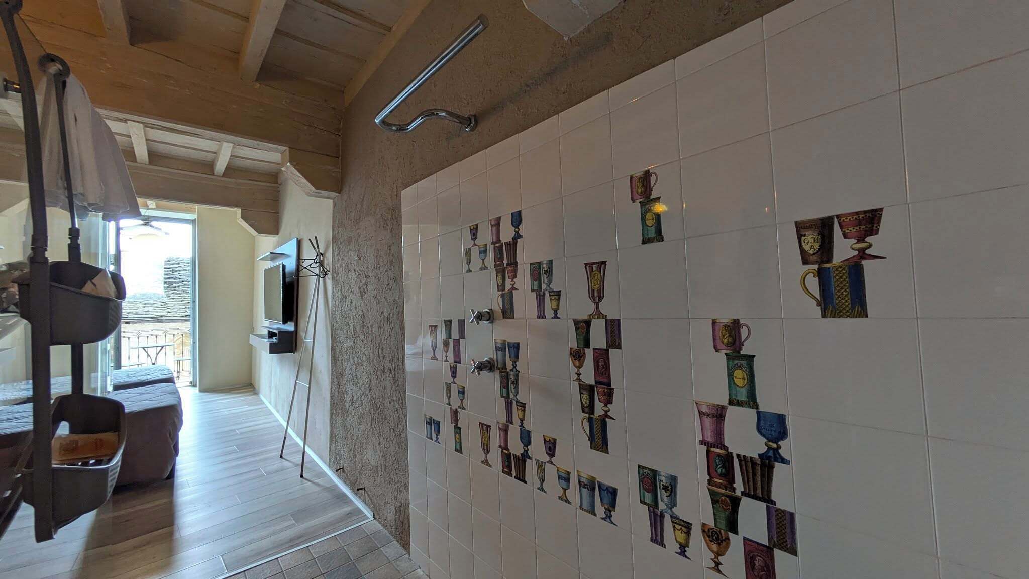 Une pièce dont un mur est recouvert de carreaux décorés de différents motifs de tasses, avec un plafond en bois et une porte visible donnant sur un autre espace.