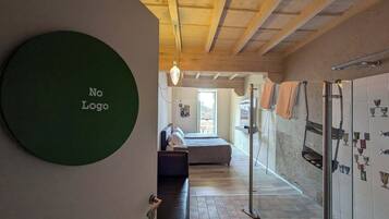 A room with a bed, a sofa, a shower area, and a wall with a 'No Logo' sign.