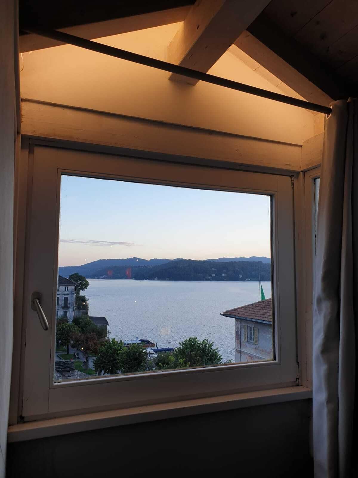 A room with a large window overlooking a lake, a building with a green flag, and a clear sky.