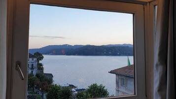 A room with a large window overlooking a lake, a building with a green flag, and a clear sky.