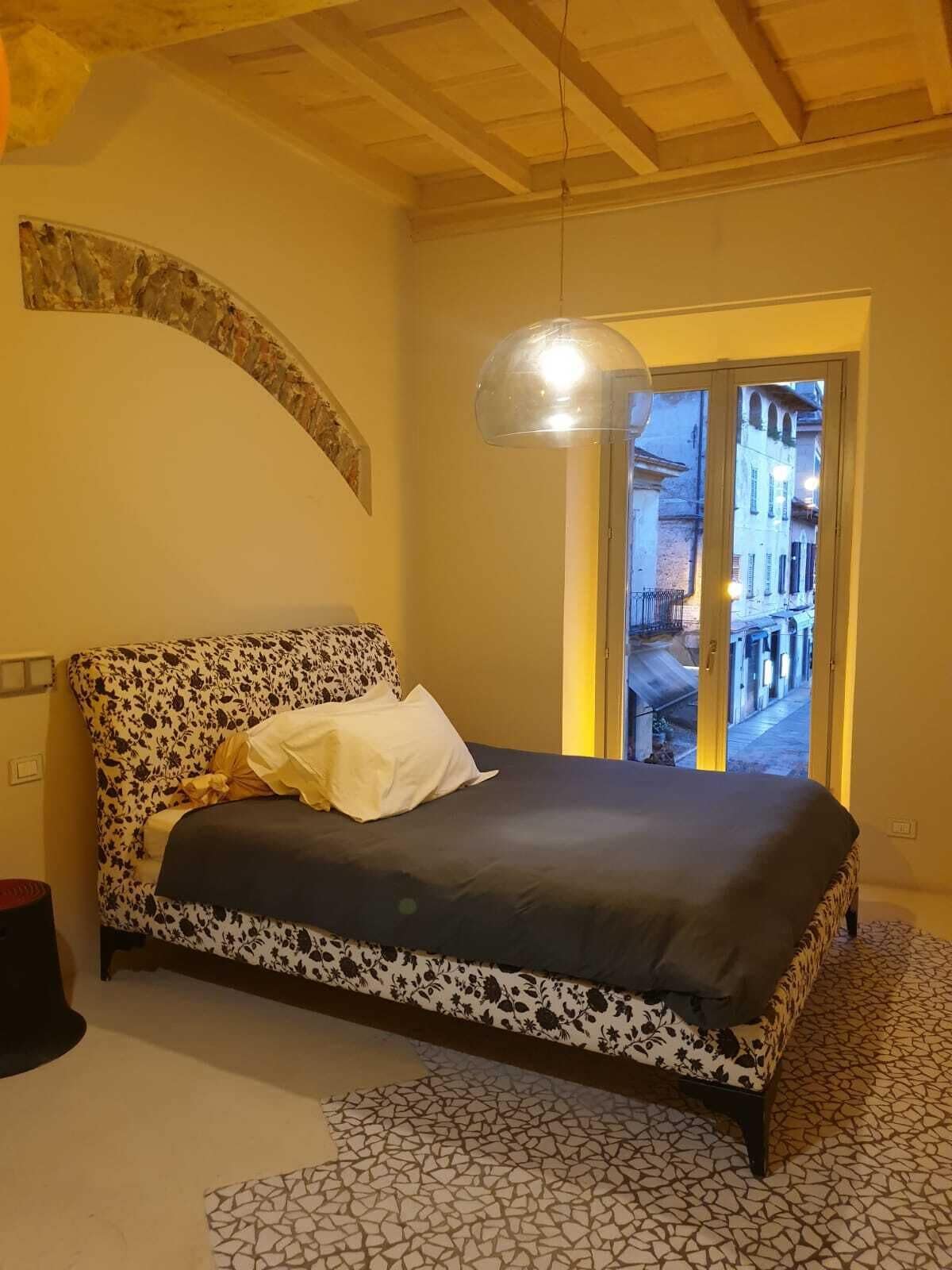 A bedroom with a patterned bed, a large window, and a unique ceiling design.