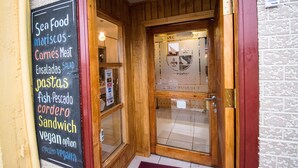 A restaurant entrance with a wooden door and a sign listing menu items like seafood, pasta, and sandwiches. - Hostal Alcazar  (Natales)