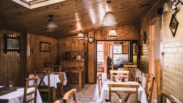 A rustic wooden interior with tables and chairs, a kitchen area, and a clock on the wall. - Hostal Alcazar  (Natales)