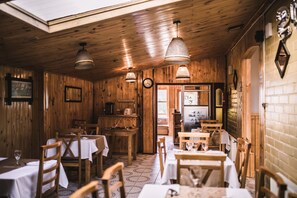 A rustic wooden interior with tables and chairs, a kitchen area, and a clock on the wall. - Hostal Alcazar  (Natales)