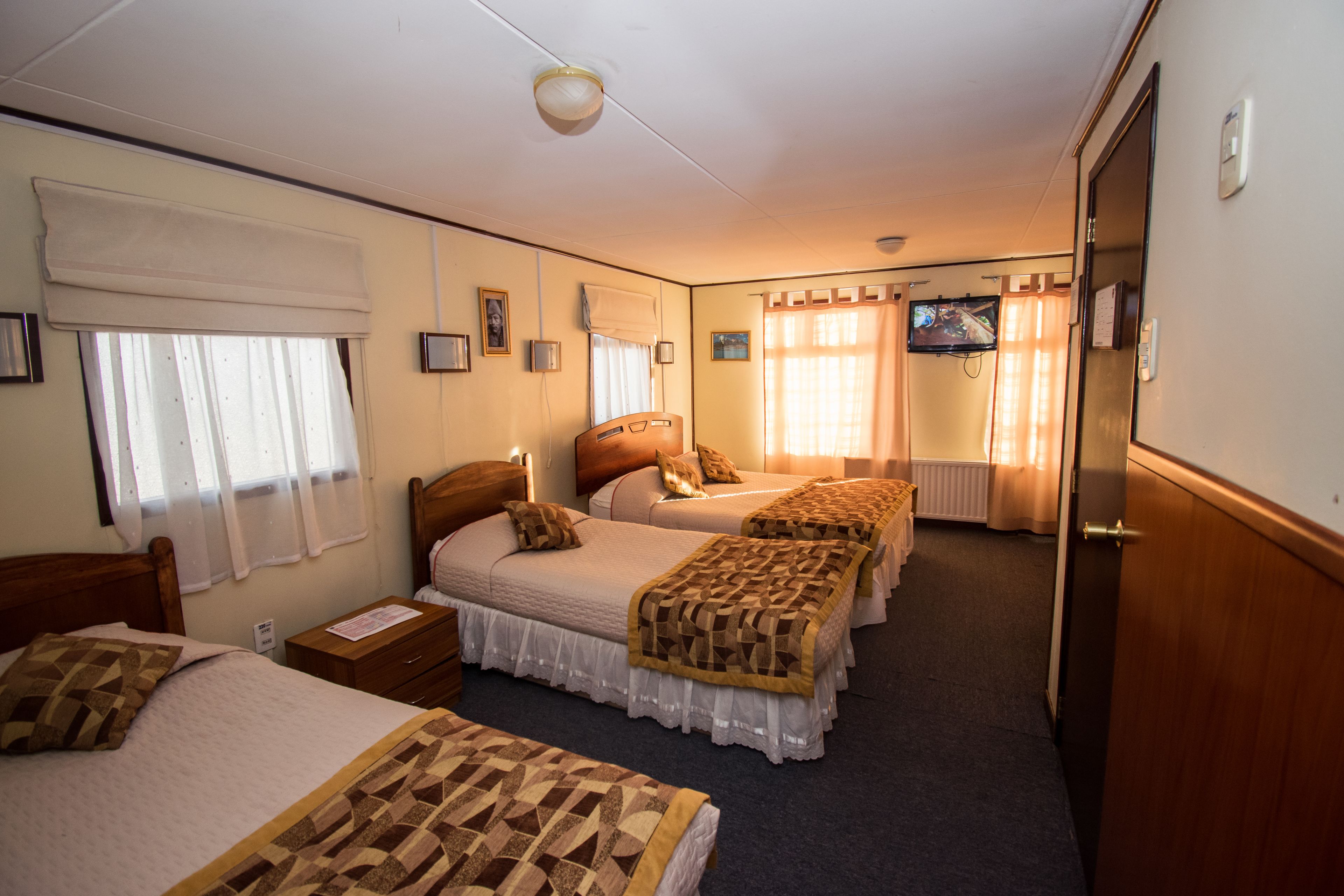 A hotel room with three beds, a television, and a window with curtains.
