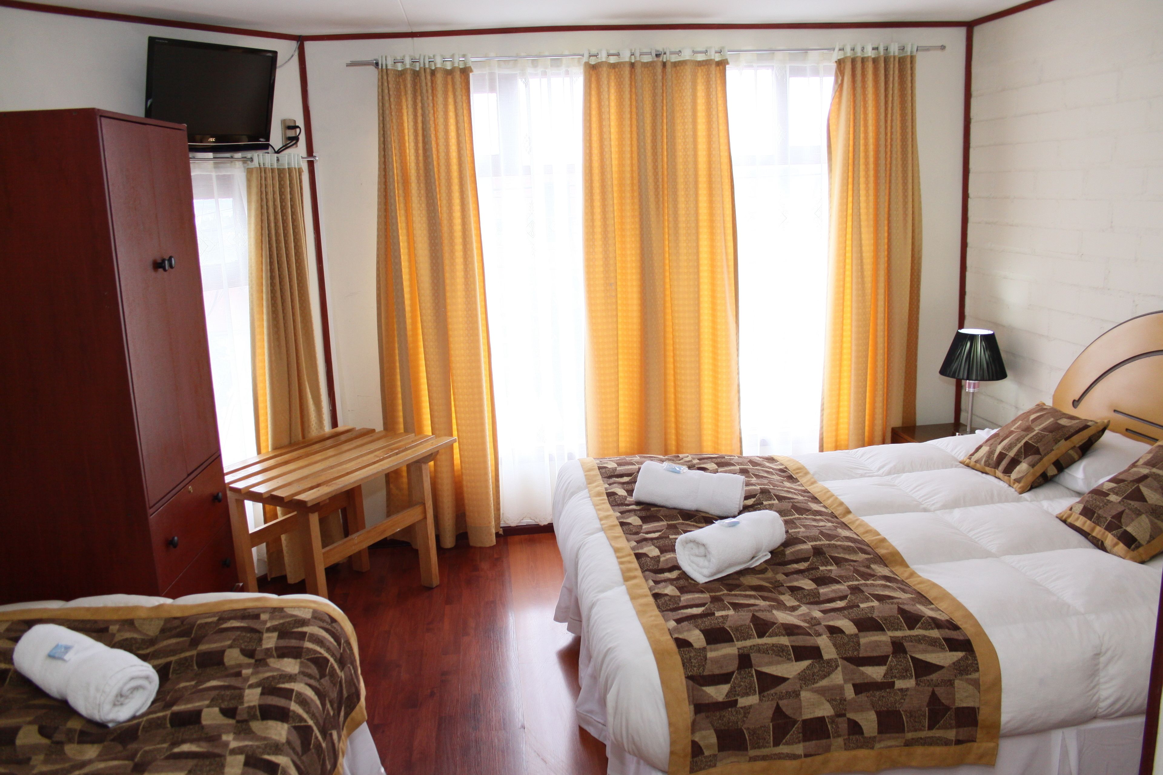 A hotel room with two beds, a wooden desk, a TV on a cabinet, and a lamp.
