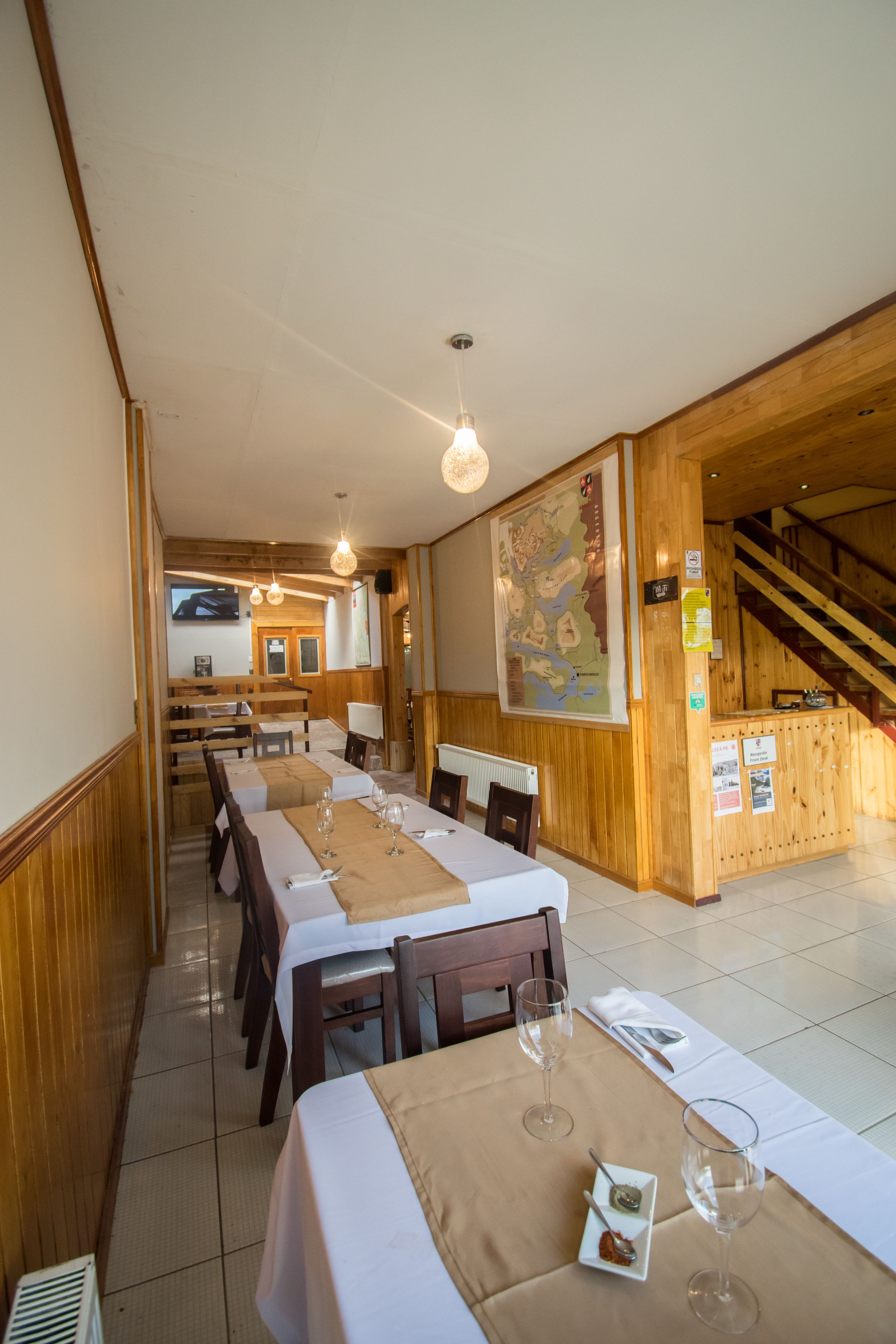 A dining area with wooden walls, a long table set with white tablecloths, wine glasses, and a menu.