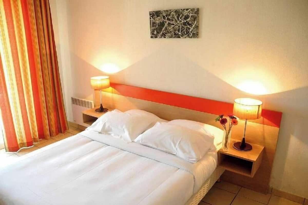 Een hotelkamer met een groot bed, twee bedlampen, een nachtkastje en een kunstwerk aan de muur.