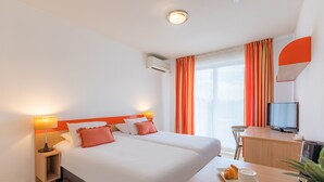 Een hotelkamer met twee bedden, een bureau met televisie, een lamp en een ontbijttafel met croissant en koffie.