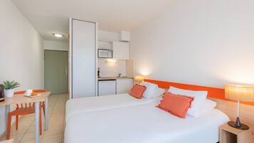 Een hotelkamer met een bed, een bureau met stoel, een klein keukentje en een badkamer.