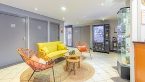 Een moderne woonkamer met een gele bank, oranje en rode stoelen, een klein houten tafeltje en een automaat.