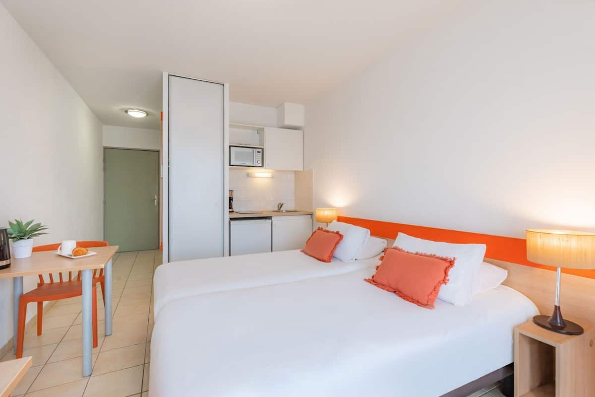 Een hotelkamer met een bed, nachtkastje, lamp en een kitchenette.