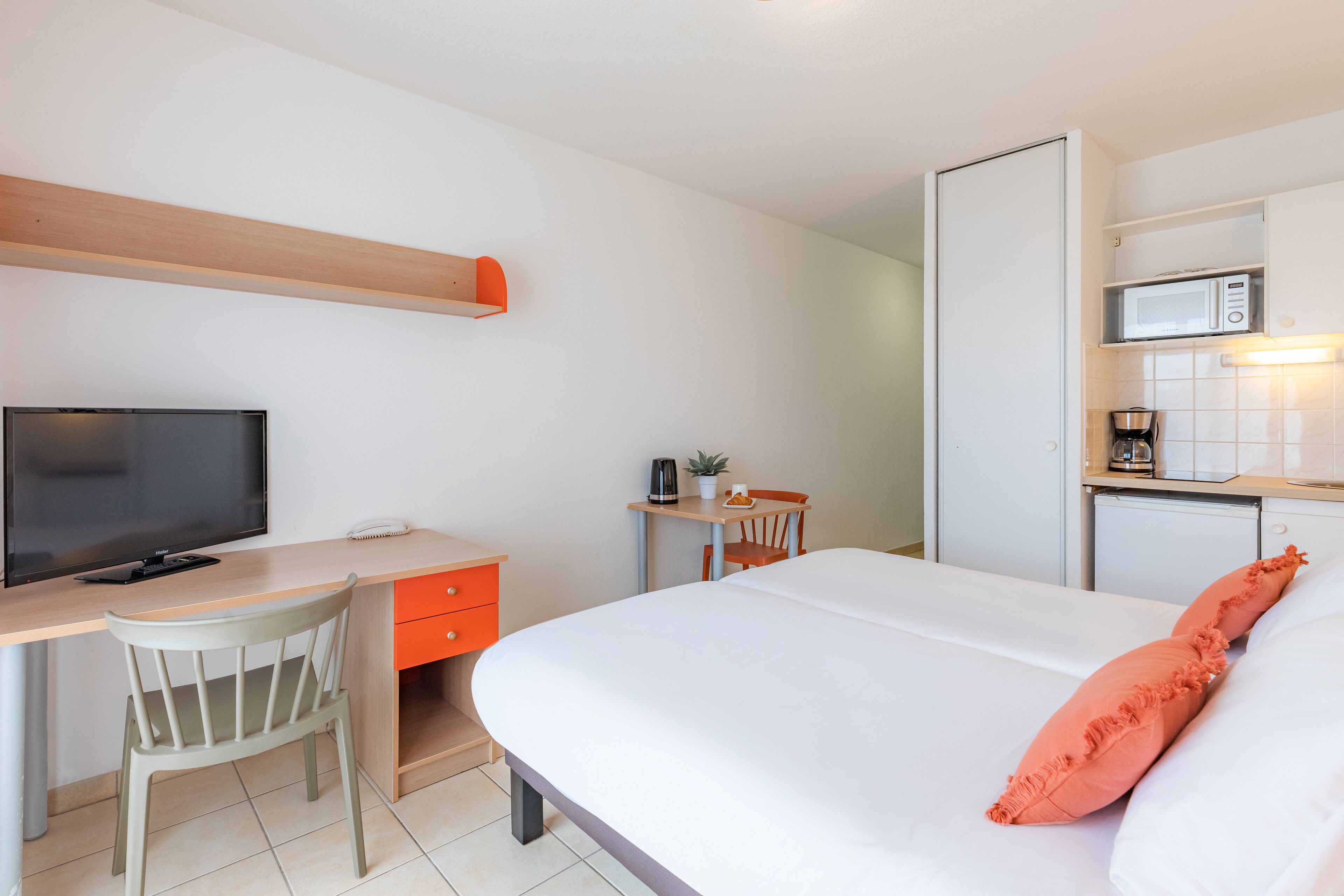 A hotel room with a bed, a desk with a chair, a television, a microwave, and a small kitchenette.