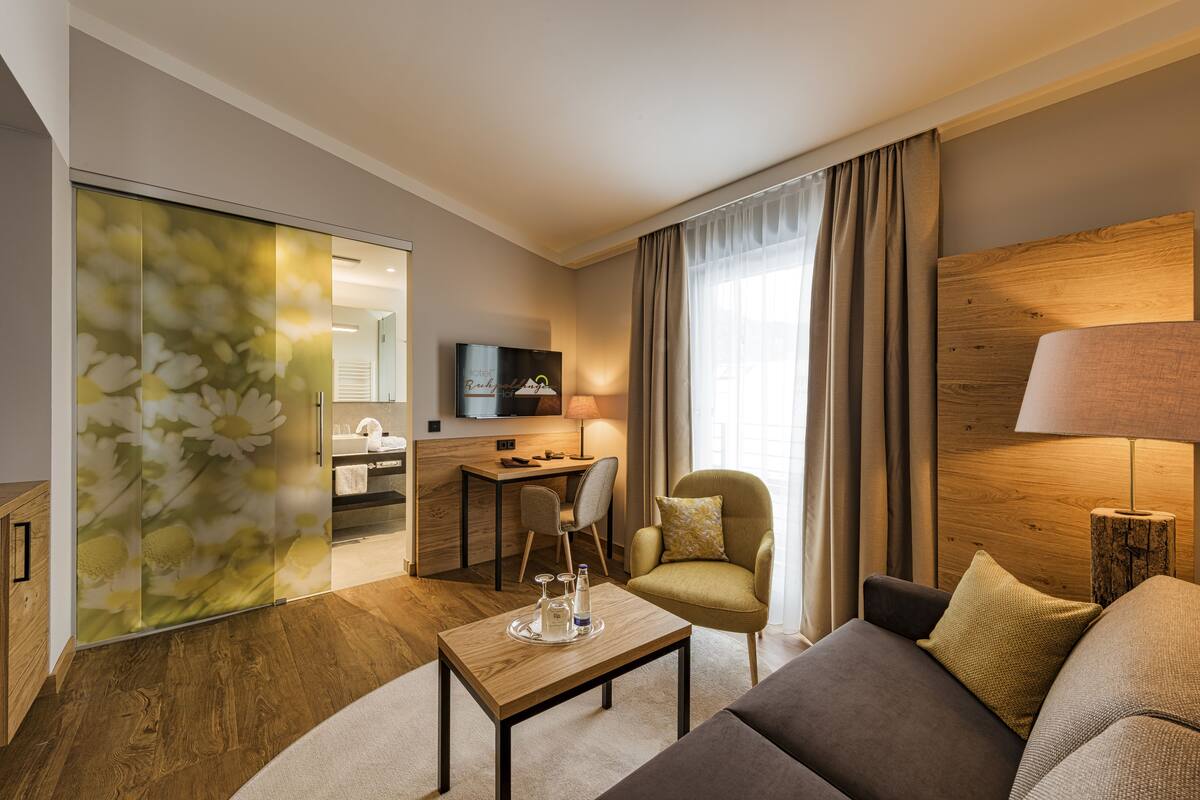 A modern hotel room with a sofa, a coffee table, a chair, a desk, and a TV.