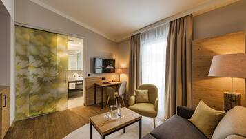 Una habitación de hotel moderna con sofá, mesa de centro, silla, escritorio y televisor.