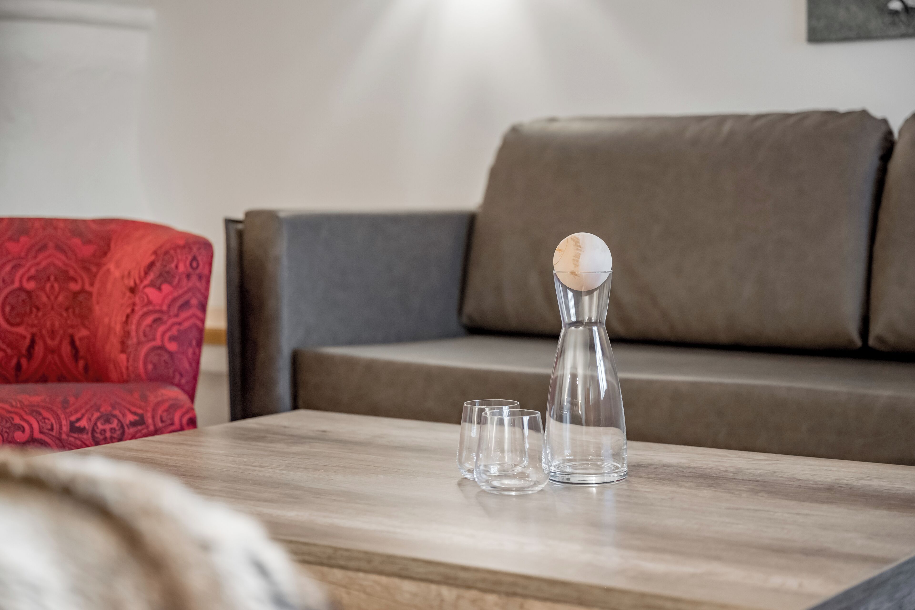Ein modernes Wohnzimmer mit einem Holztisch, einer transparenten Karaffe und zwei Gläsern.