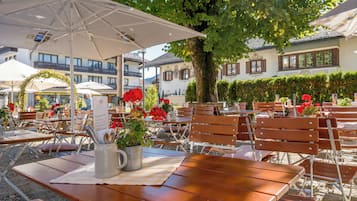 An outdoor seating area with wooden tables and chairs, umbrellas, and potted plants.