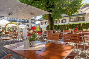 An outdoor seating area with wooden tables and chairs, umbrellas, and potted plants.