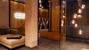 A modern interior with a sofa, a wooden partition, and pendant lighting. - Ruhpoldinger Hof (Ruhpolding)