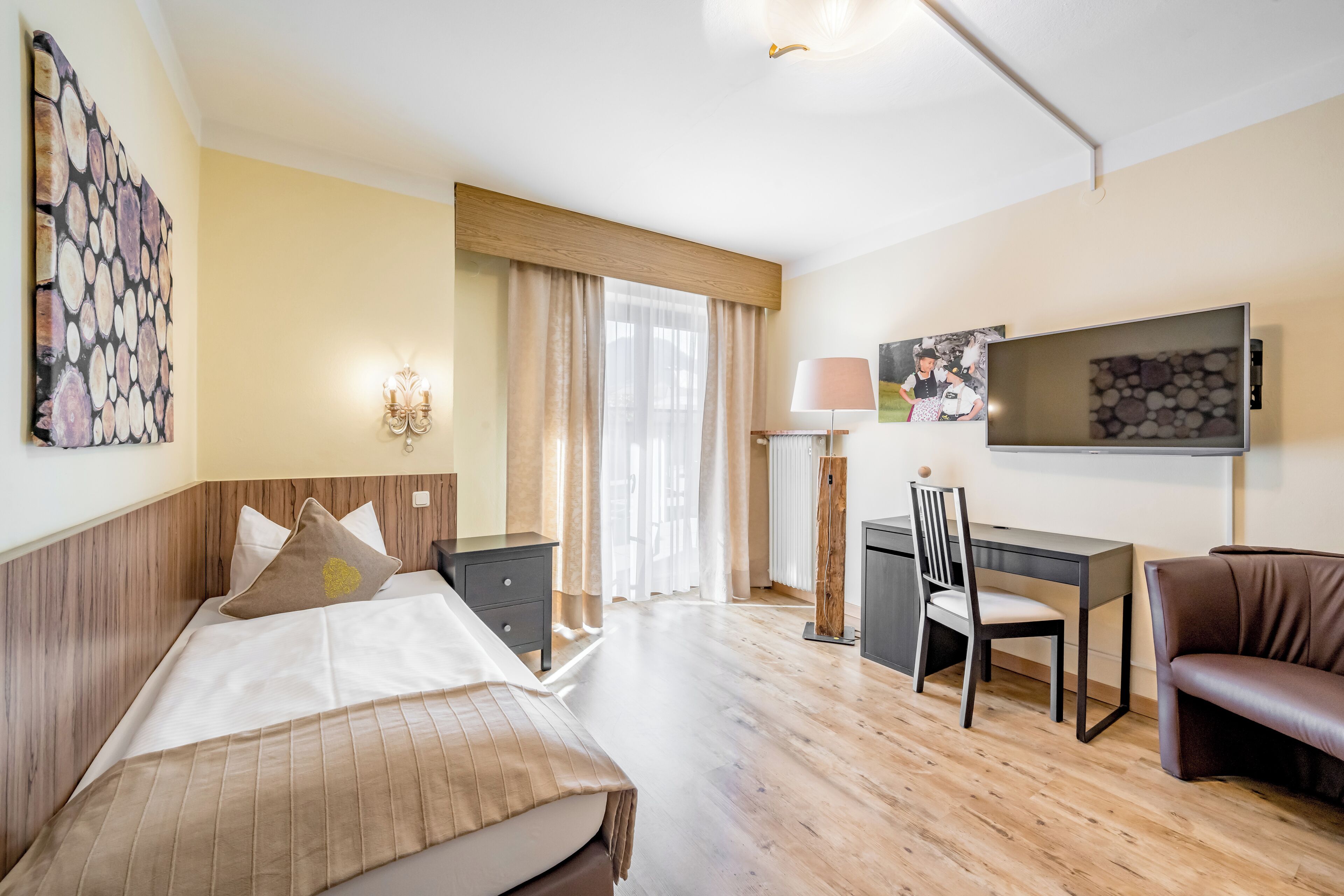 Een hotelkamer met een bed, bureau, stoel en een televisie aan de muur.