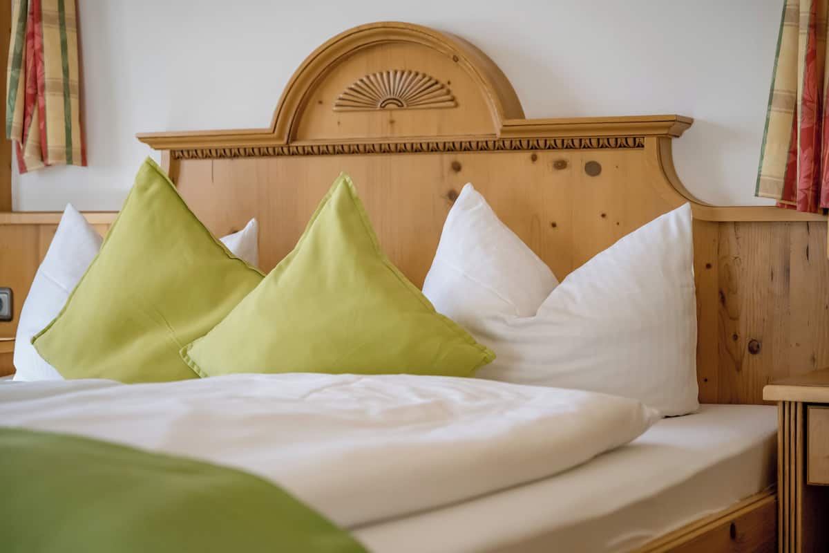 A neatly made bed with white and green pillows, a wooden headboard with a sun design, and a wooden nightstand with a lamp.