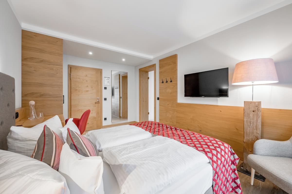 A hotel room with a large bed, a TV mounted on the wall, a lamp, and a wooden headboard.