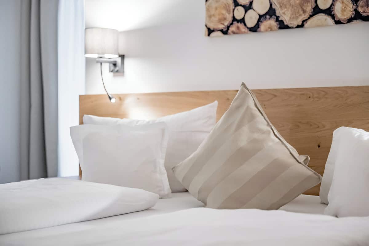A neatly made bed with white and striped pillows, a wooden headboard, and a wall-mounted lamp.