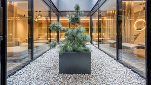 A modern indoor garden with a central tree, surrounded by glass walls and a pebble floor. - Ruhpoldinger Hof (Ruhpolding)