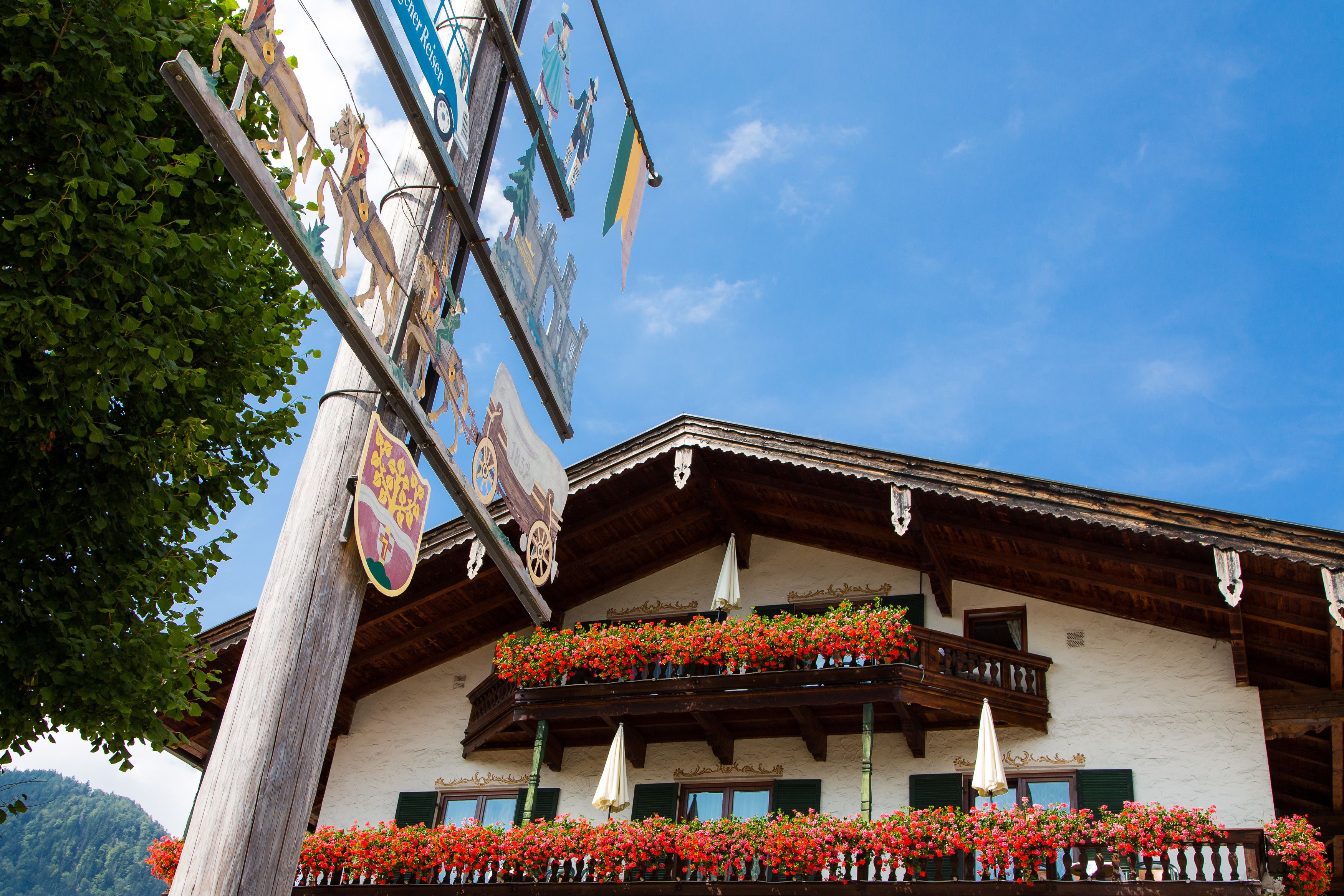 A traditional building with a balcony adorned with red flowers, wooden balconies, and a signboard with various symbols.