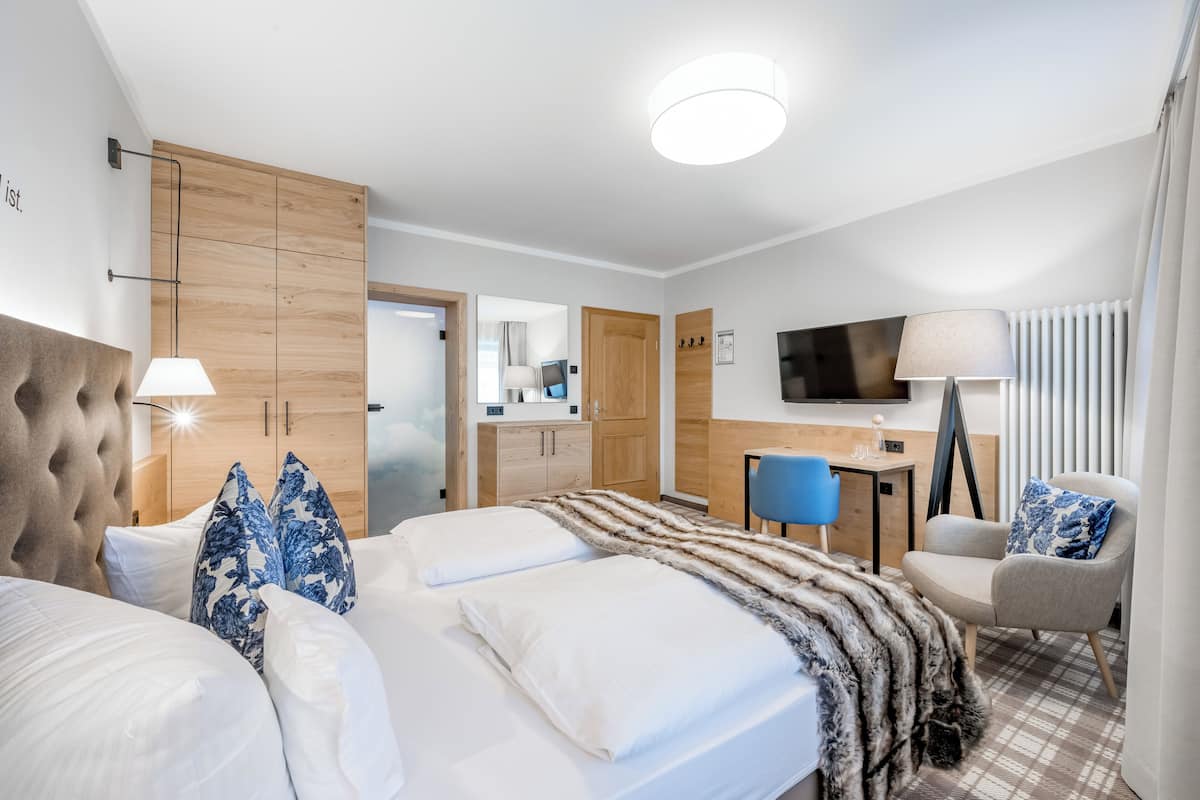 A modern hotel room with a large bed, a desk, a chair, and a television.