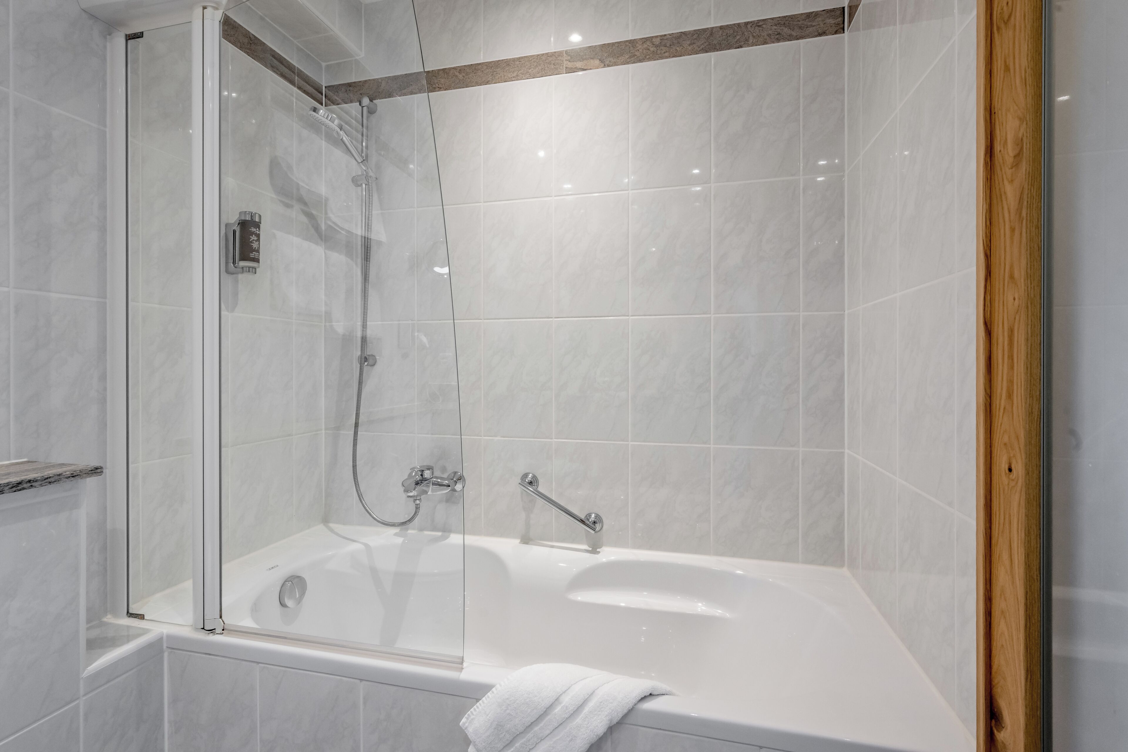 Un baño moderno con ducha envuelta en vidrio, una bañera blanca y un detalle de madera.