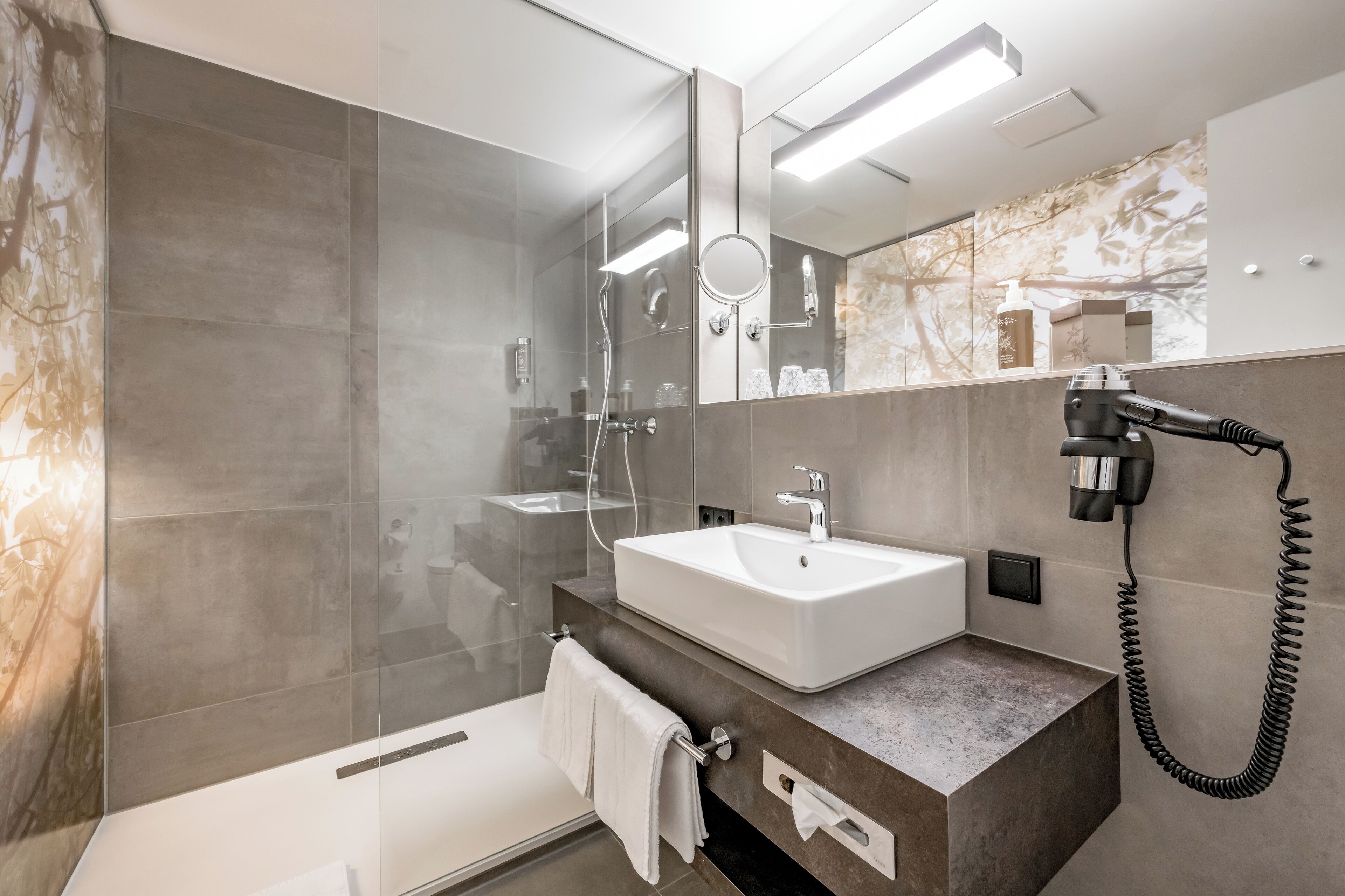 A modern bathroom with a glass shower enclosure, a white sink, and a hairdryer mounted on the wall.
