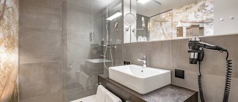 A modern bathroom with a glass shower enclosure, a white sink, and a hairdryer mounted on the wall.