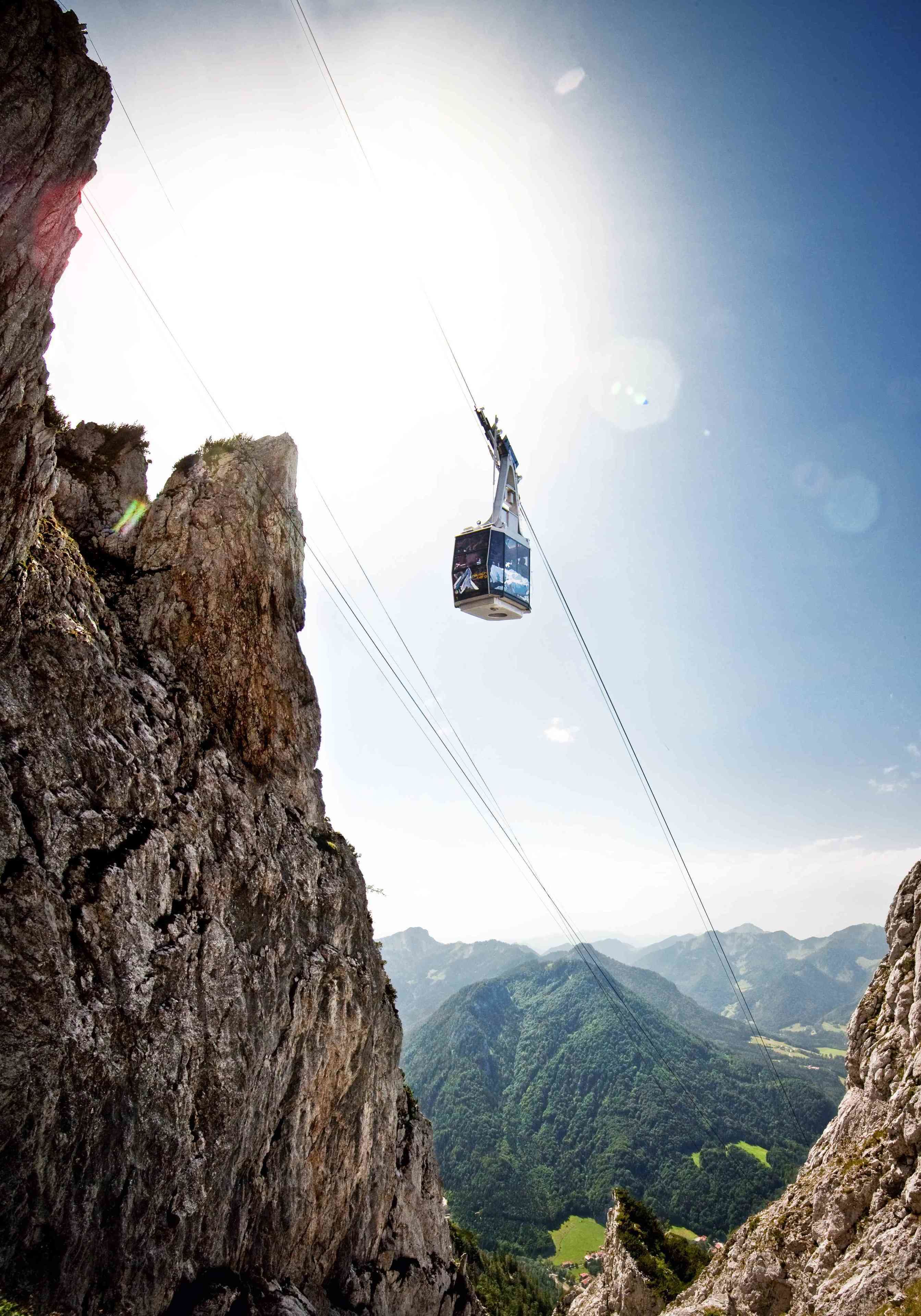A cable car suspended between rocky cliffs with a mountainous landscape in the background.